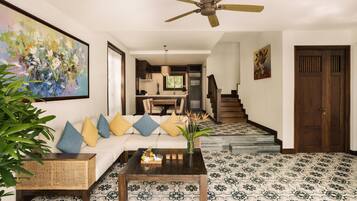 A spacious living area with a white sofa, a coffee table, and a ceiling fan. A staircase leads to an upper floor.
