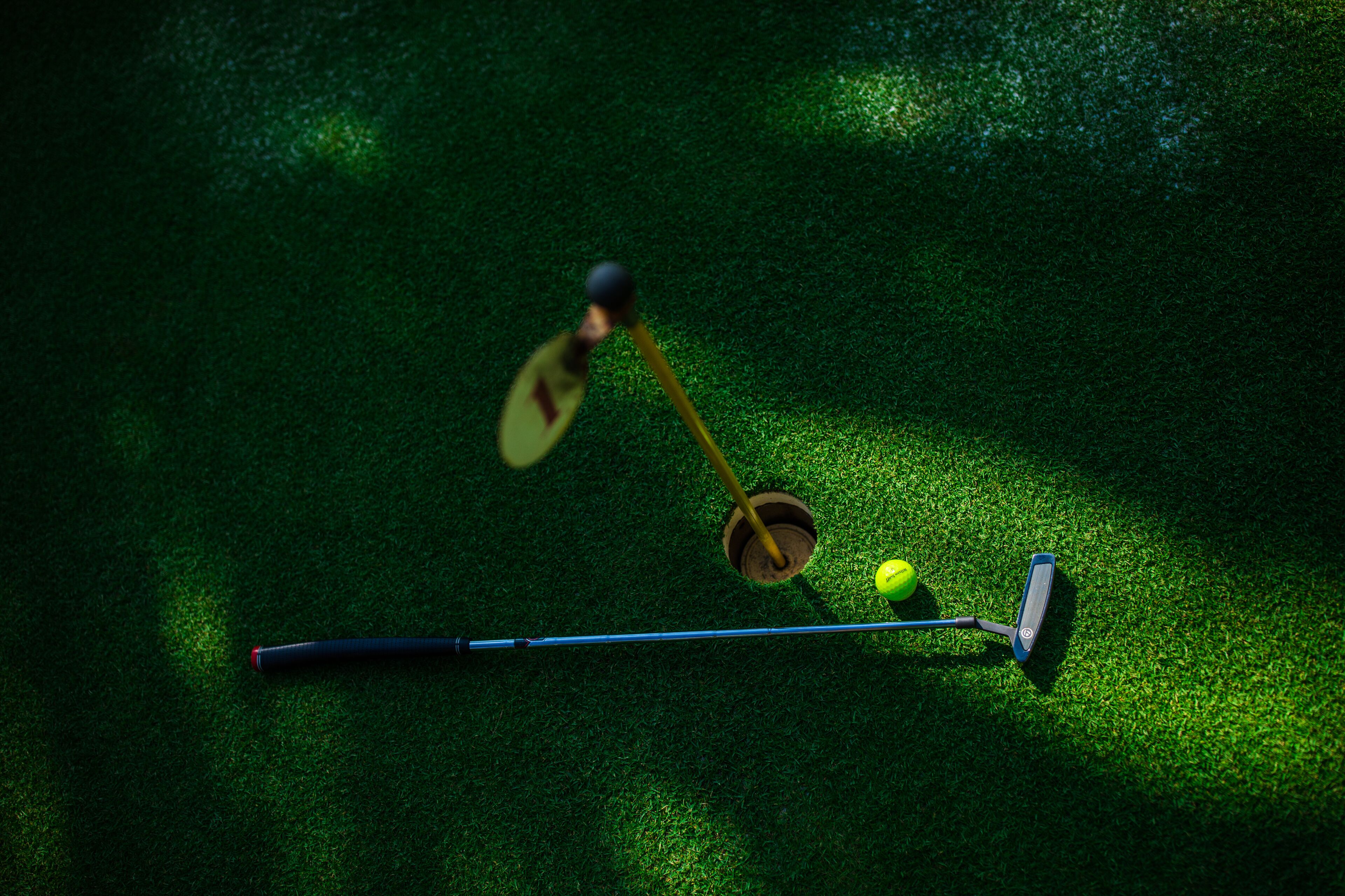 Een golfclub, een bal en een putter op een groene ondergrond.