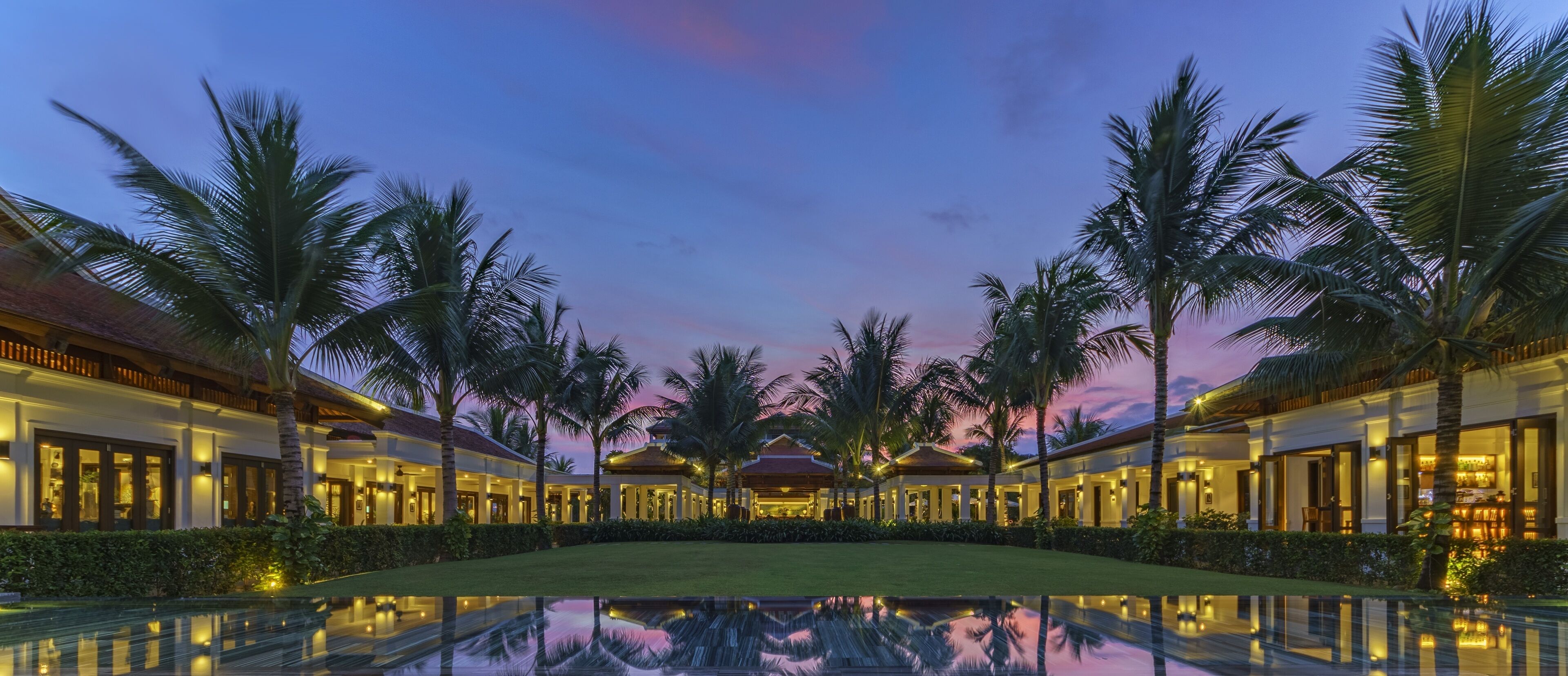A resort with a reflective pool, palm trees, and buildings with warm lighting.