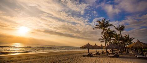 Ein Strand mit Palmen, Sonnenschirmen und Liegestühlen.