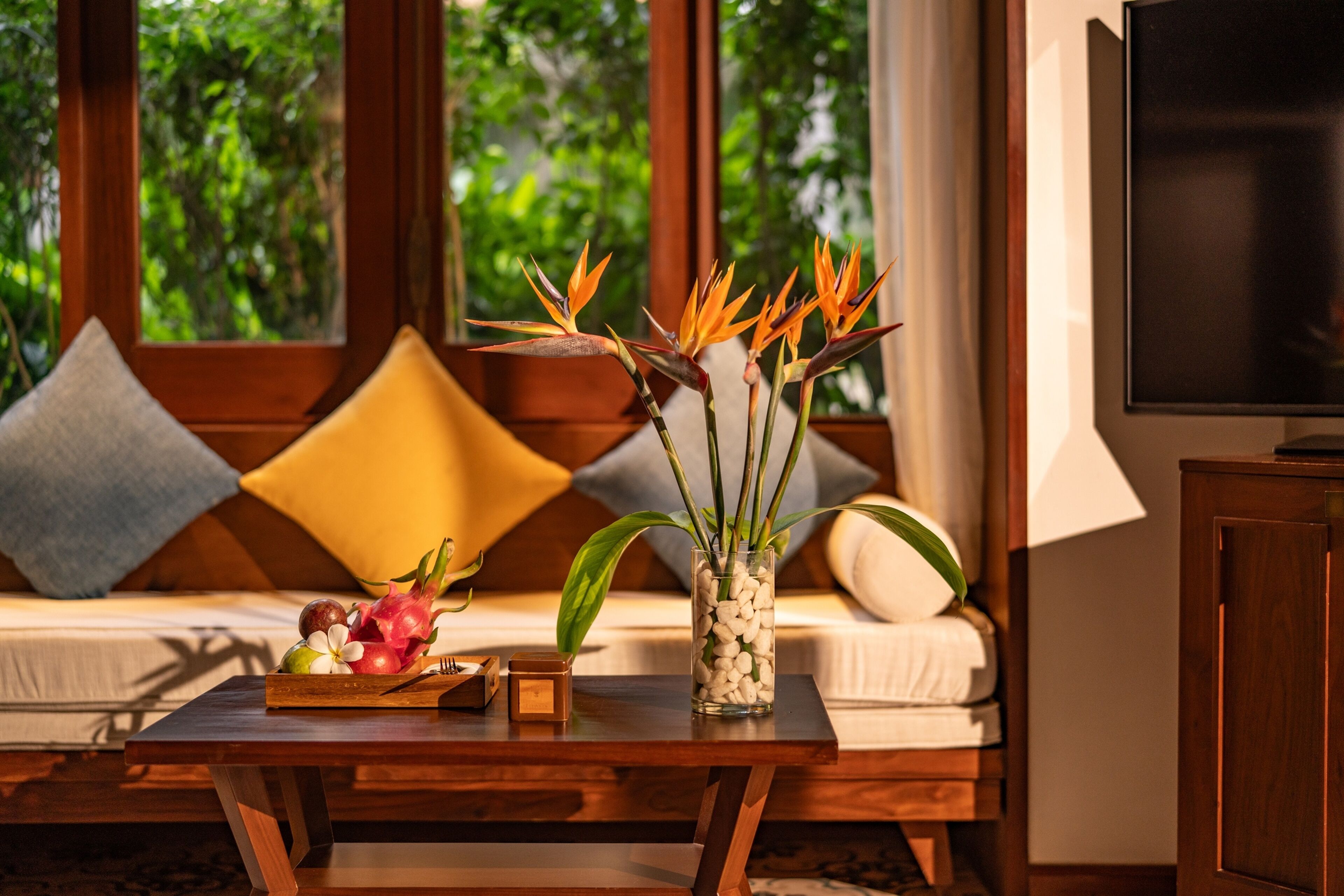 A wooden coffee table with a vase of flowers and a fruit bowl.