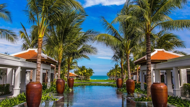 A pool with large vases, palm trees, and a view of the ocean. - The Anam Cam Ranh (Cam Lam)
