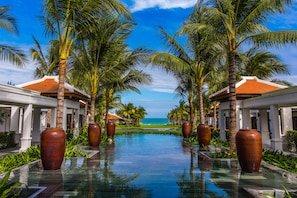 A pool with large vases, palm trees, and a view of the ocean. - The Anam Cam Ranh (Cam Lam)