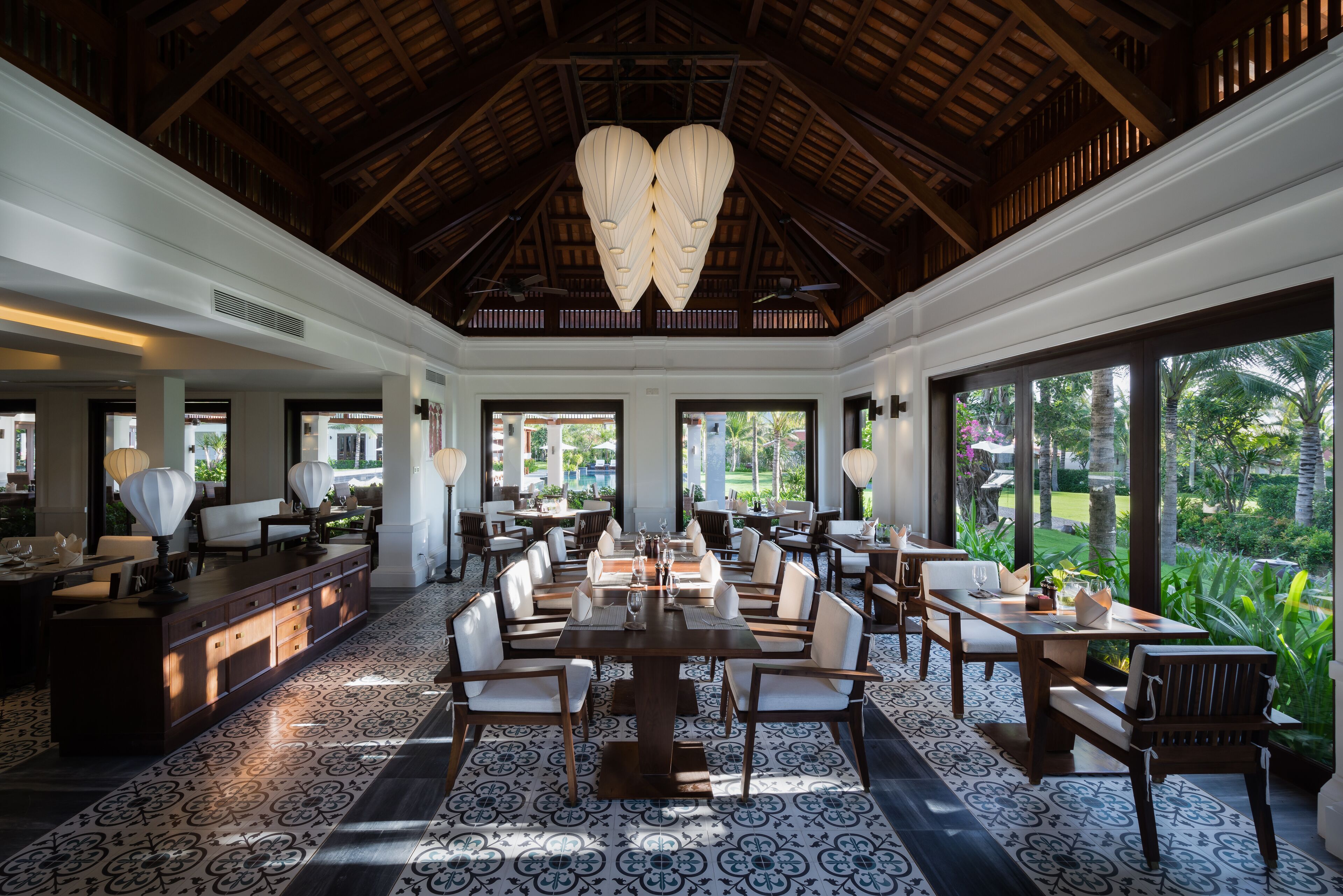 A spacious dining area with a high ceiling, large windows, and a view of the outdoors.