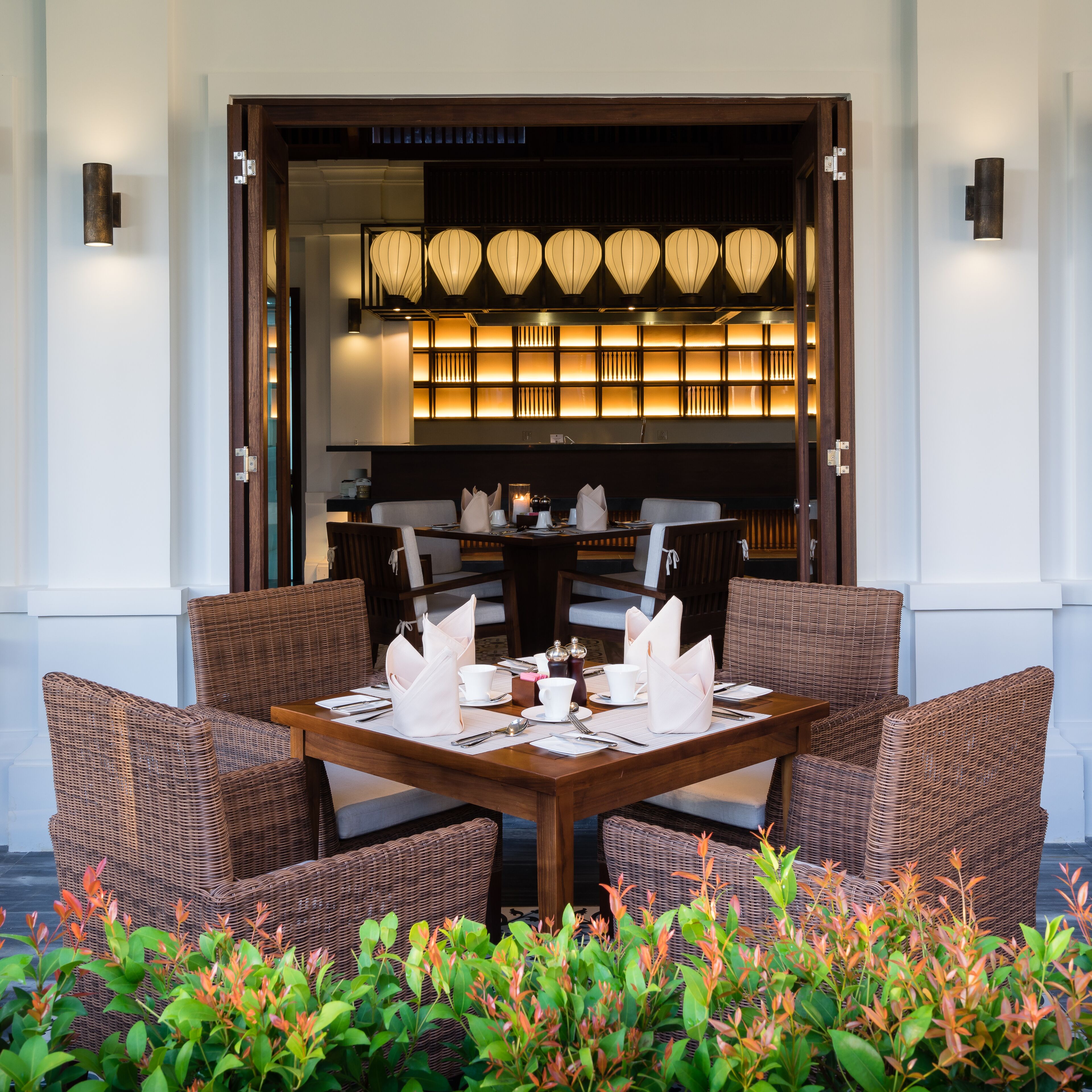 A dining area with a wooden table set for four, surrounded by wicker chairs, and a backdrop of traditional lanterns.