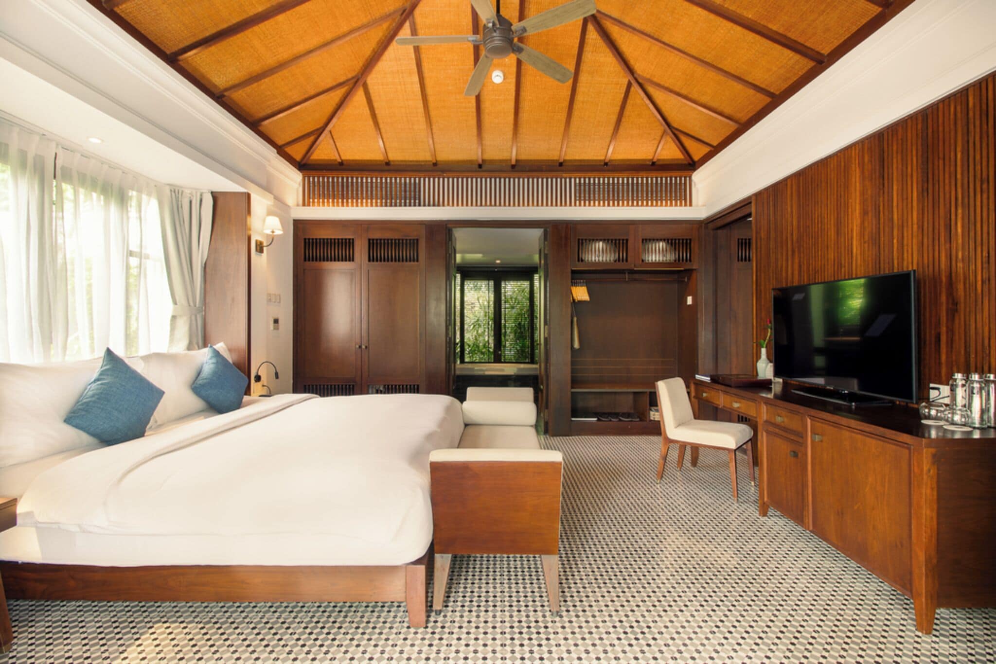 A spacious bedroom with a large bed, a TV, and a wooden ceiling.