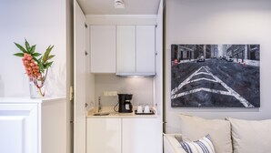 A compact kitchen with white cabinets, a coffee maker, and a sink. A painting of a city street is on the wall.