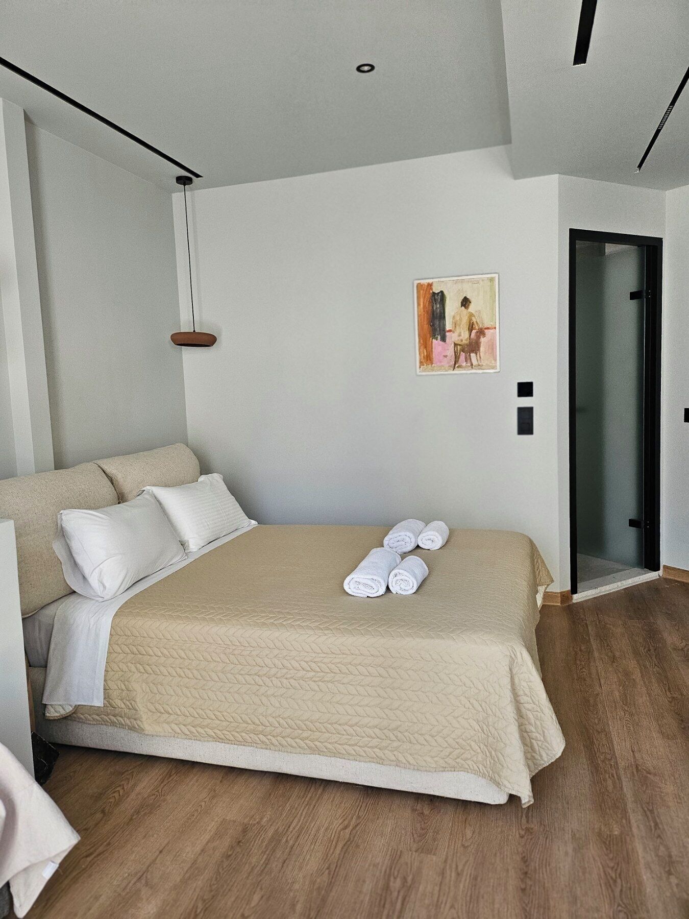 A modern bedroom with a large bed, a painting on the wall, and a door leading to another room.