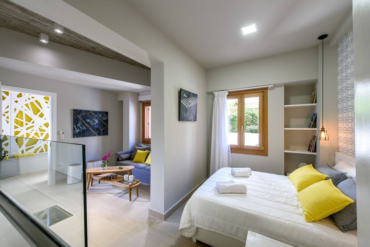 Une chambre d’hôtel moderne dotée d’un grand lit, d’un coin salon avec un canapé et des fauteuils, d’une table à manger et d’une rambarde en verre donnant sur la pièce.