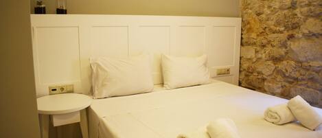 A hotel room with a bed, two pillows, a round bedside table, and a stone wall.