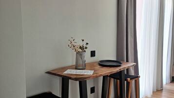 Un petit coin repas avec une table en bois, deux tabourets noirs et un vase contenant des fleurs séchées.