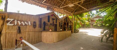 Une structure rustique en bois, dotée d’un toit de chaume et portant l’inscription « Ziwa », qui comprend un comptoir d’accueil et un petit espace porche.