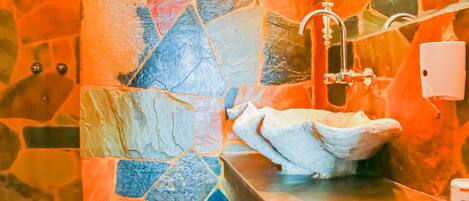 Un baño con pared de mosaicos, un lavamanos y un espejo.