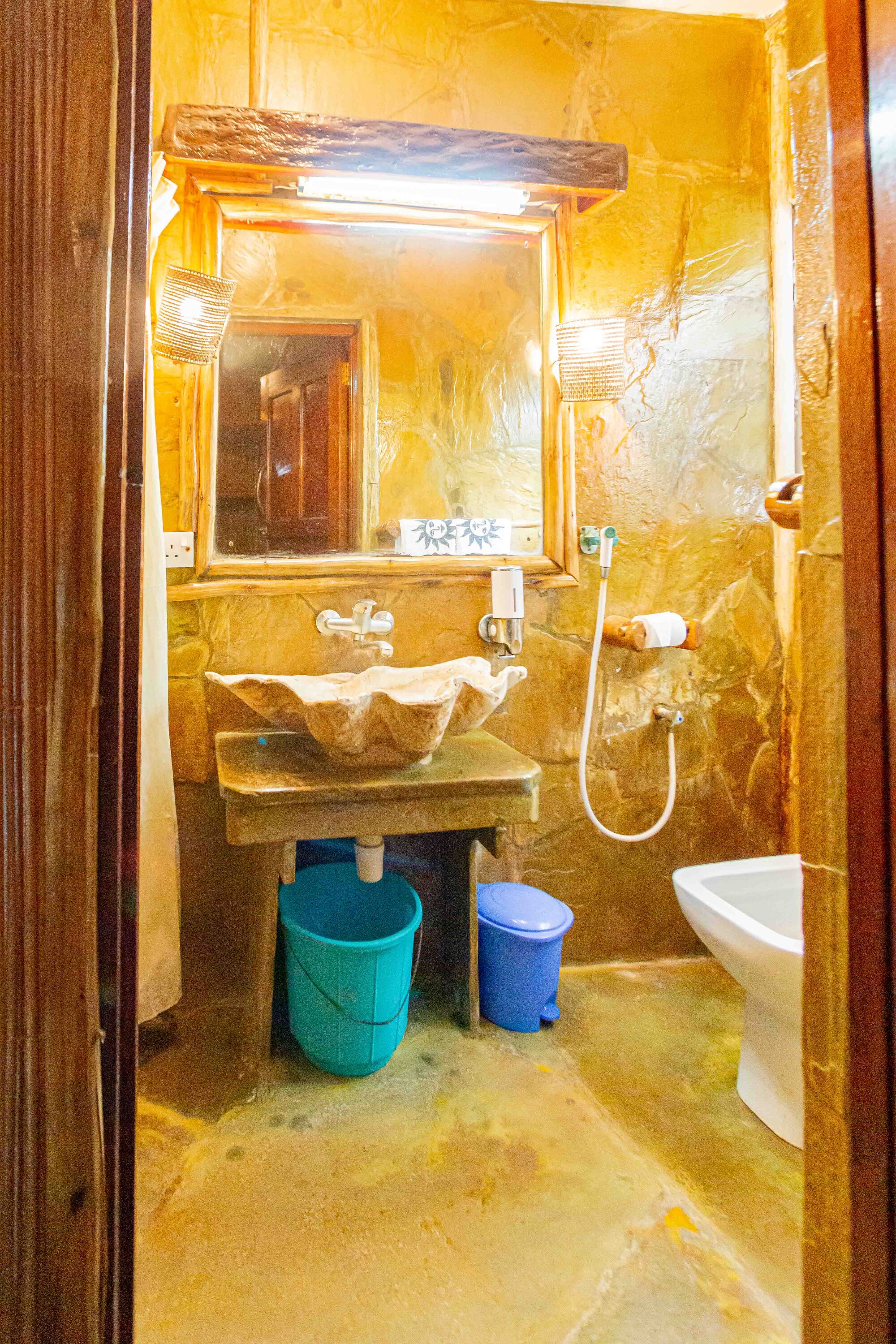 A bathroom with a stone sink, a mirror, a toilet, and a blue bucket.
