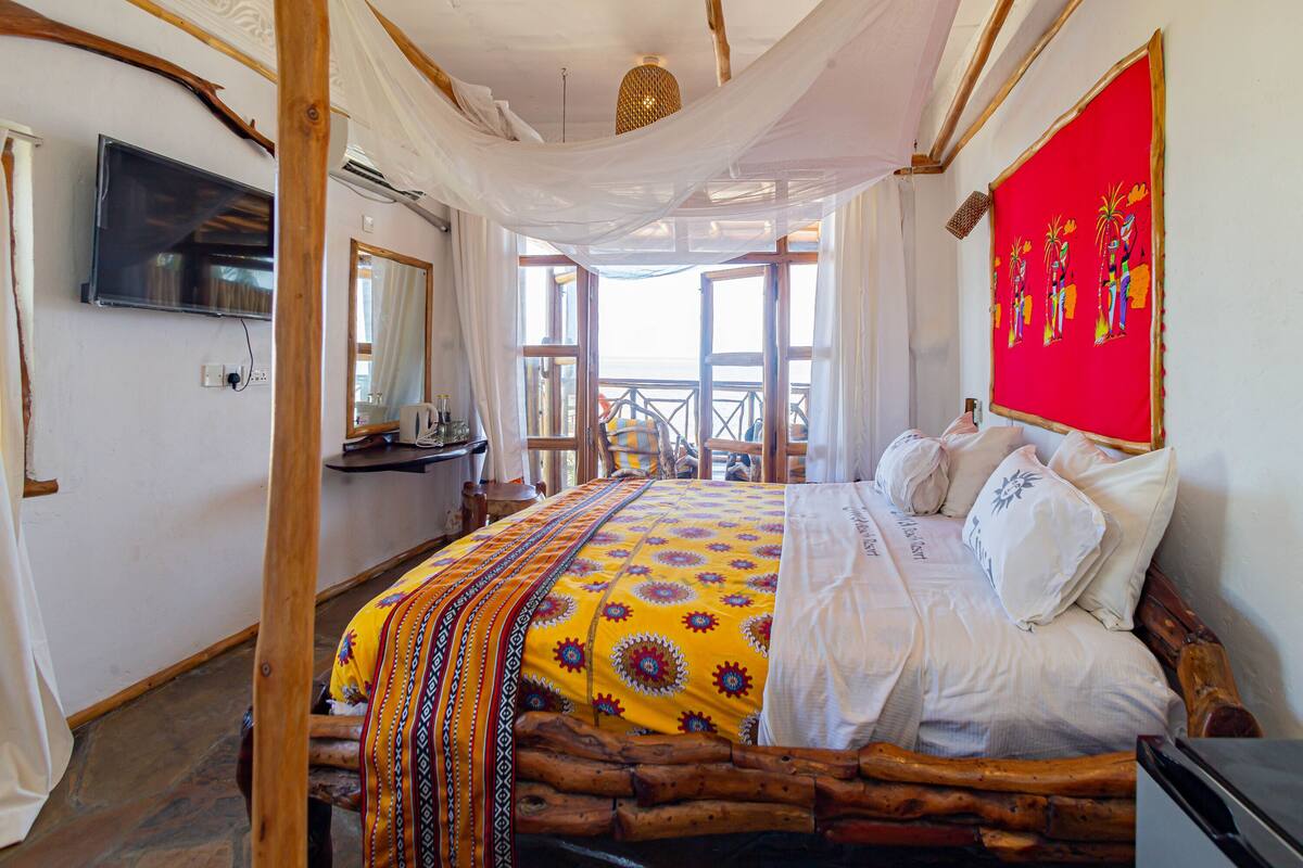 A room with a bed, a television, a mirror, and a window with a view.