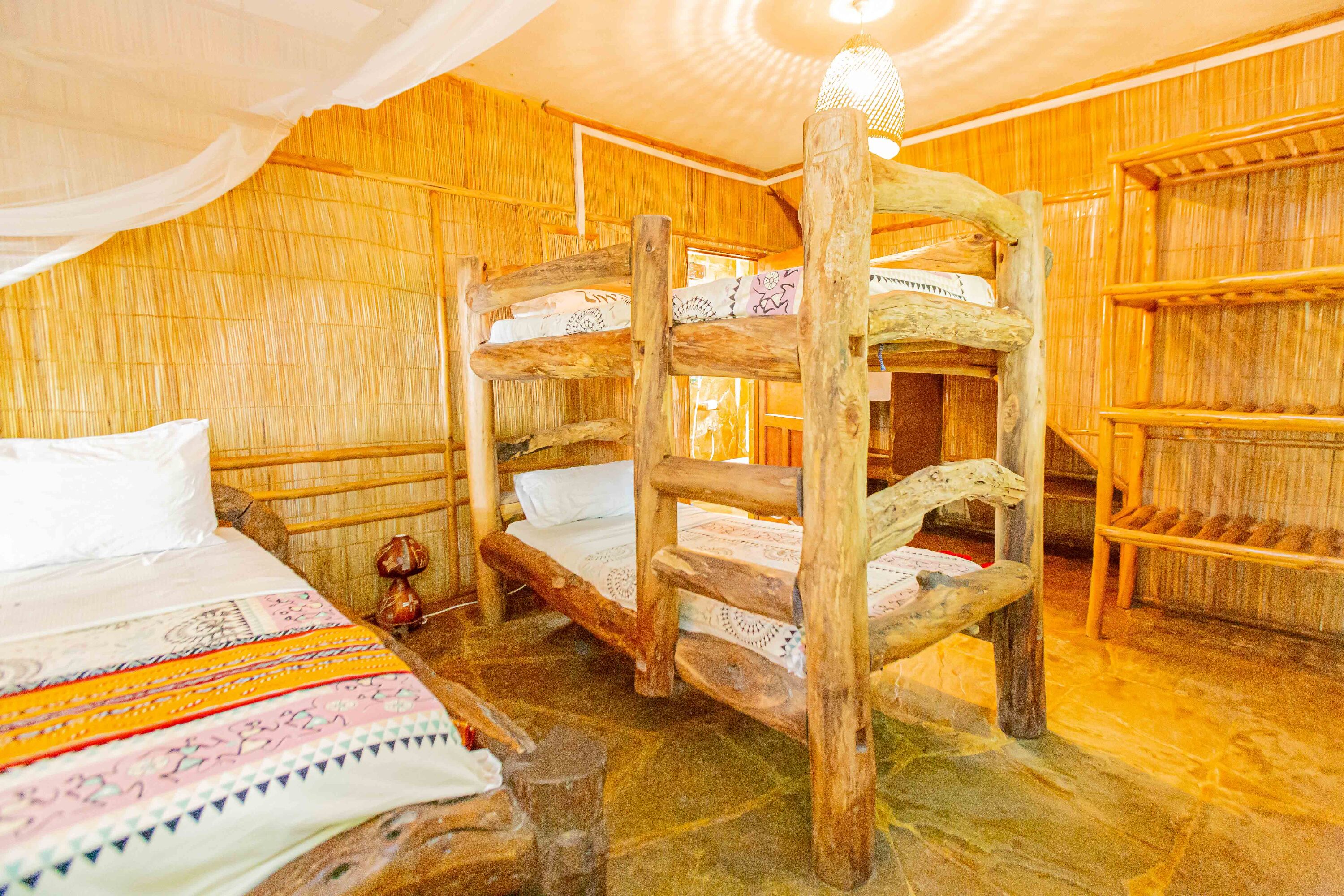 A rustic wooden room with bunk beds and a single bed, featuring a woven wall and a hanging light fixture.