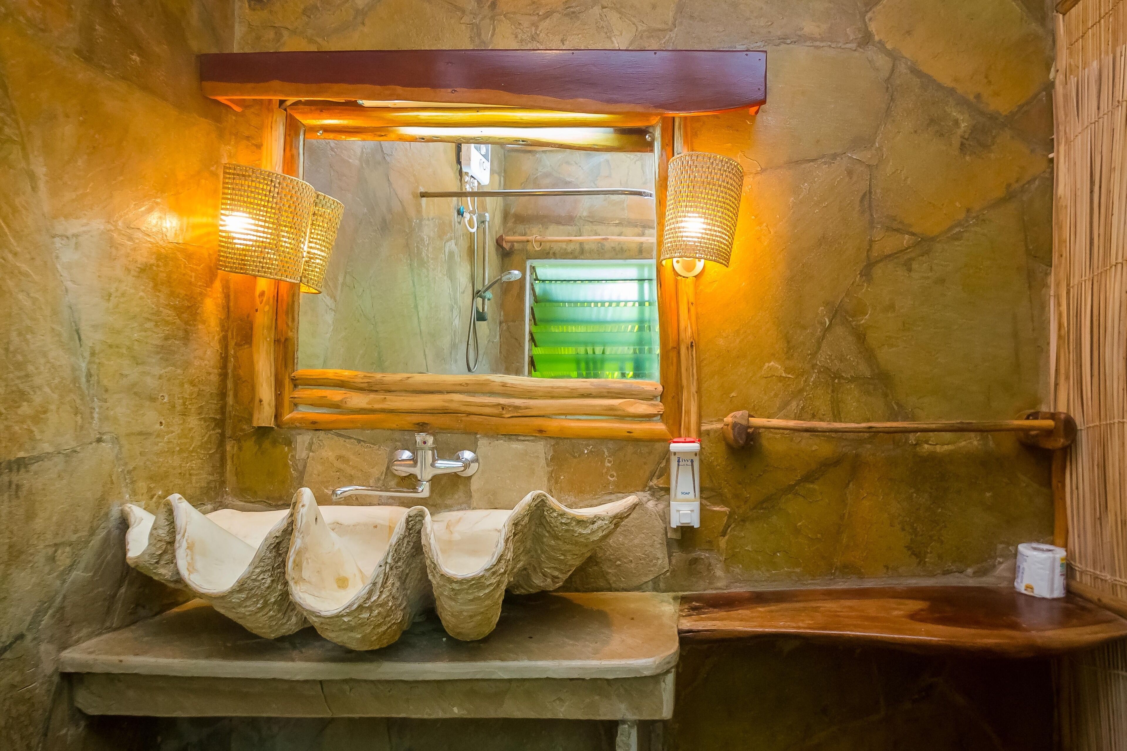 Un baño con pared de piedra, un estante de madera, un lavabo con un diseño original y dos luces empotradas.
