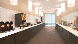 A modern kitchen with a long countertop, coffee machines, a microwave, and a large window offering a view. - La Quinta Inn & Suites by Wyndham Cleveland near Lee Univ (Cleveland)