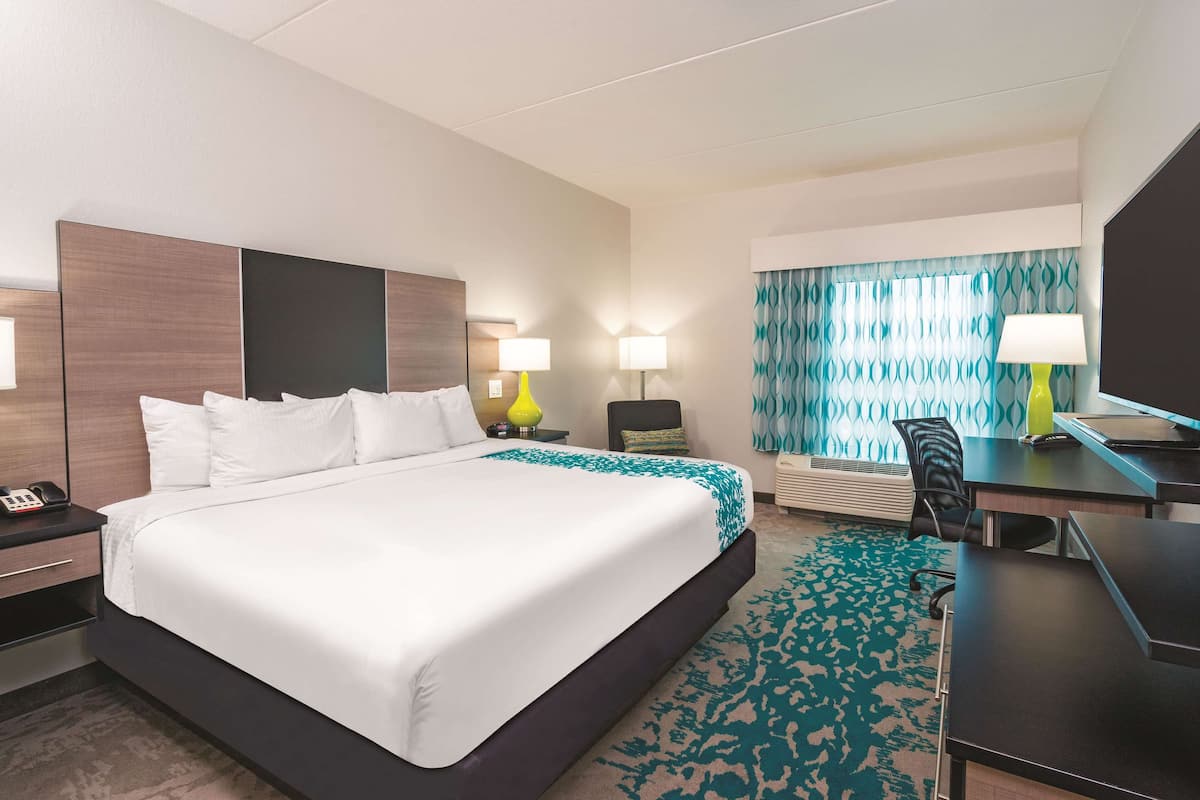 A hotel room with a large bed, bedside tables, a desk with a chair, a television, and a window with curtains.