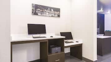 A modern office space with two desks, each with a computer and keyboard, and a printer on one of the desks. There is a framed cityscape artwork on the wall above the desks.