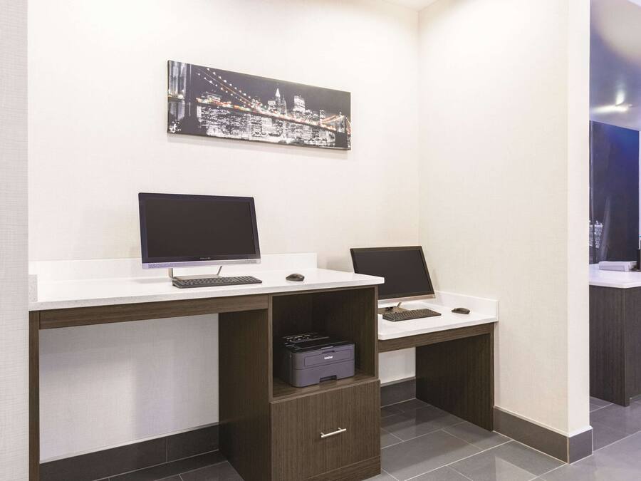 A modern office space with two desks, each with a computer and keyboard, and a printer on one of the desks. There is a framed cityscape artwork on the wall above the desks.