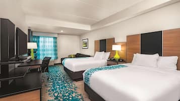 Une chambre d’hôtel avec deux lits, un bureau, une chaise, une lampe de bureau, une table de chevet et un tableau au mur.