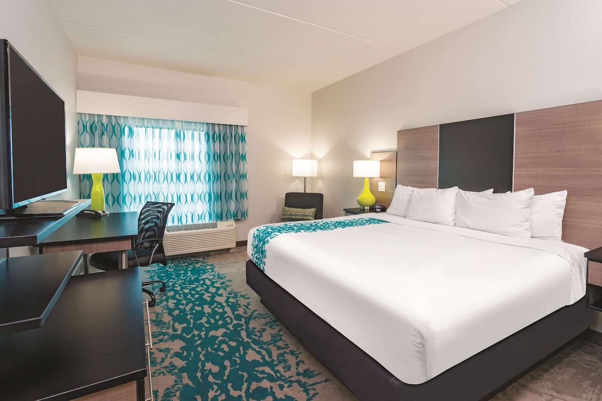 A hotel room with a large bed, a desk with a chair, two lamps, and a television.