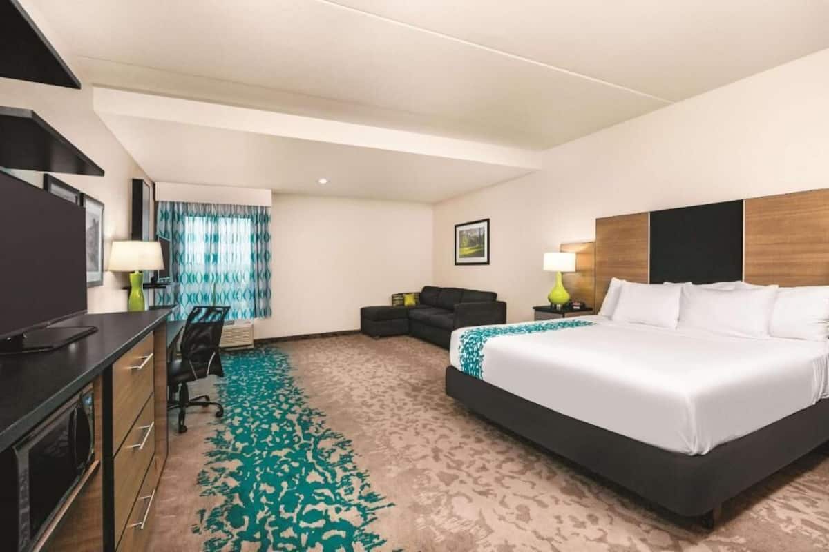 A hotel room with a bed, desk, chair, and a view of the outdoors.