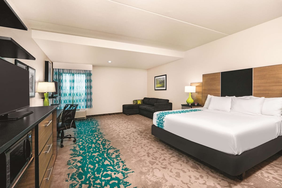A hotel room with a large bed, a desk with a chair, a sofa, and a TV.