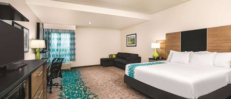 Quarto de hotel com uma cama grande, uma escrivaninha com cadeira, um sofá e uma televisão.