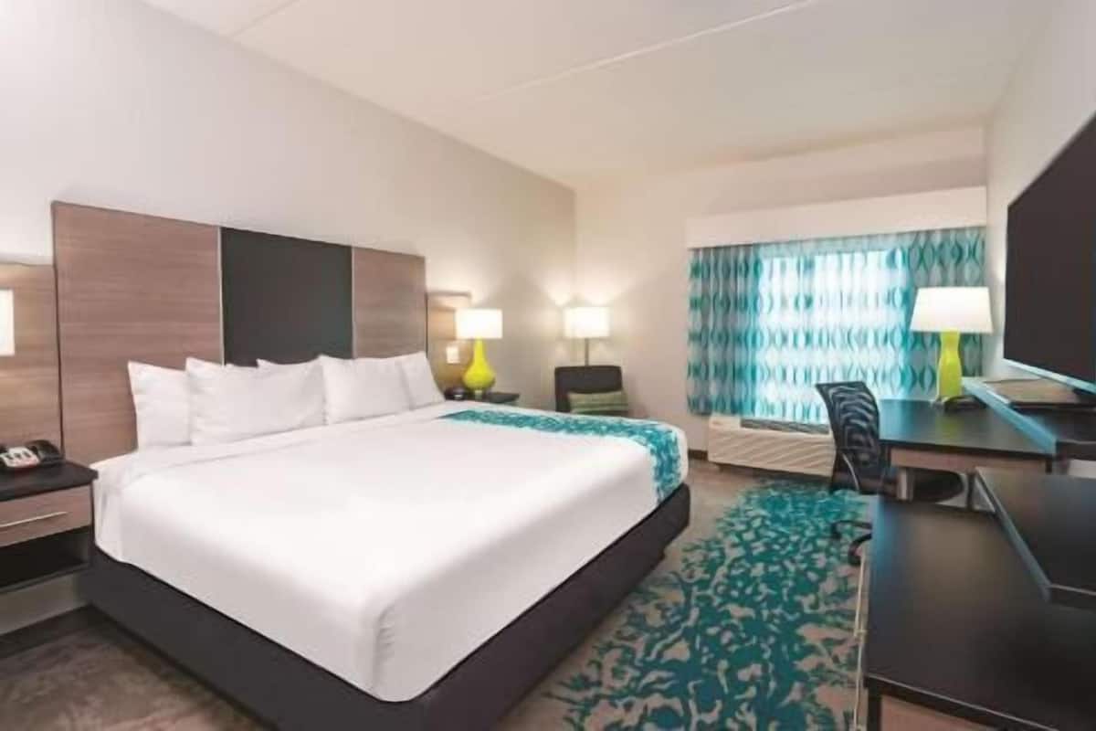 A hotel room with a large bed, a desk with a chair, a television, and a window with curtains.