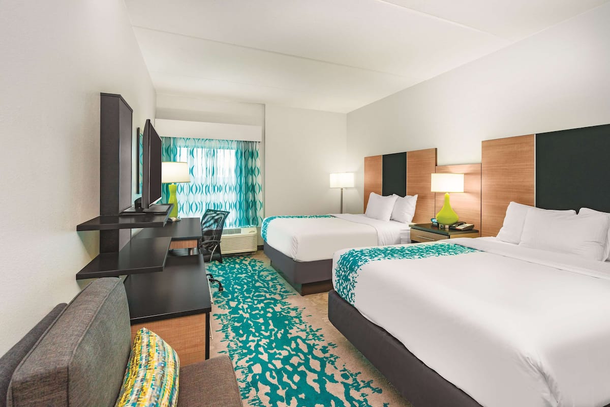 A hotel room with two beds, a desk, a chair, a TV, and a window with curtains.