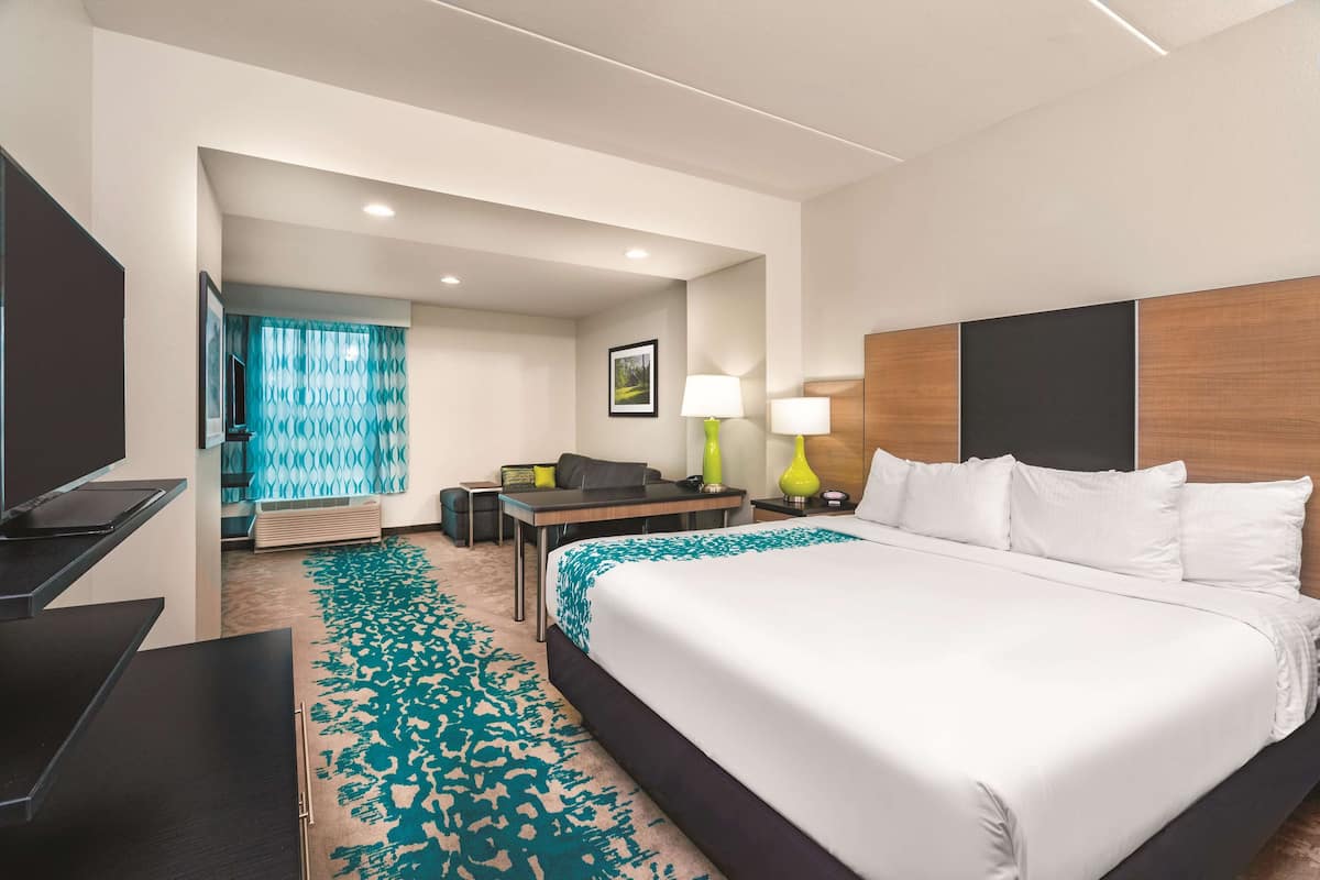 A hotel room with a large bed, a desk with a chair, a TV, and a bathroom with a shower and toilet.