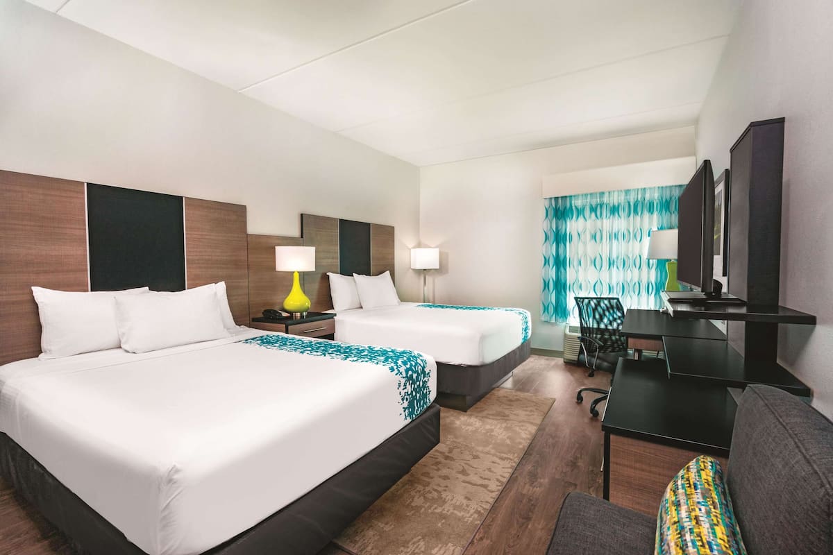 A hotel room with two beds, a desk, a chair, a TV, and a window with curtains.