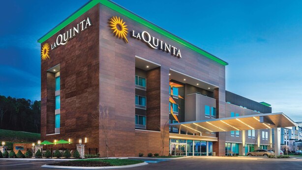 A La Quinta hotel with a modern design, featuring a prominent sun logo and a covered entrance. - La Quinta Inn & Suites by Wyndham Cleveland near Lee Univ (Cleveland)