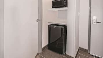 Una kitchenette compacta con un microondas en un estante, un refrigerador pequeño y un lavavajillas.
