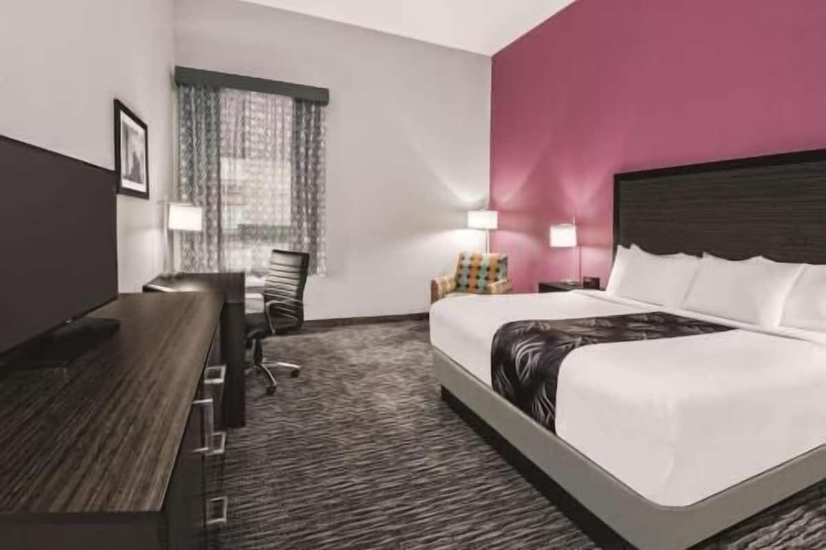 A hotel room with a bed, a desk, a chair, a lamp, and a window with curtains.