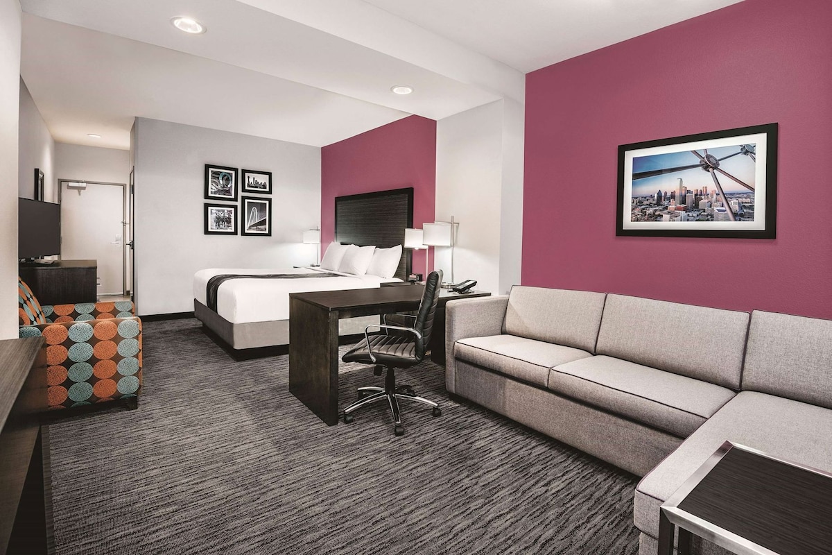 A hotel room with a bed, a desk, a sofa, a chair, and a cityscape picture on the wall.