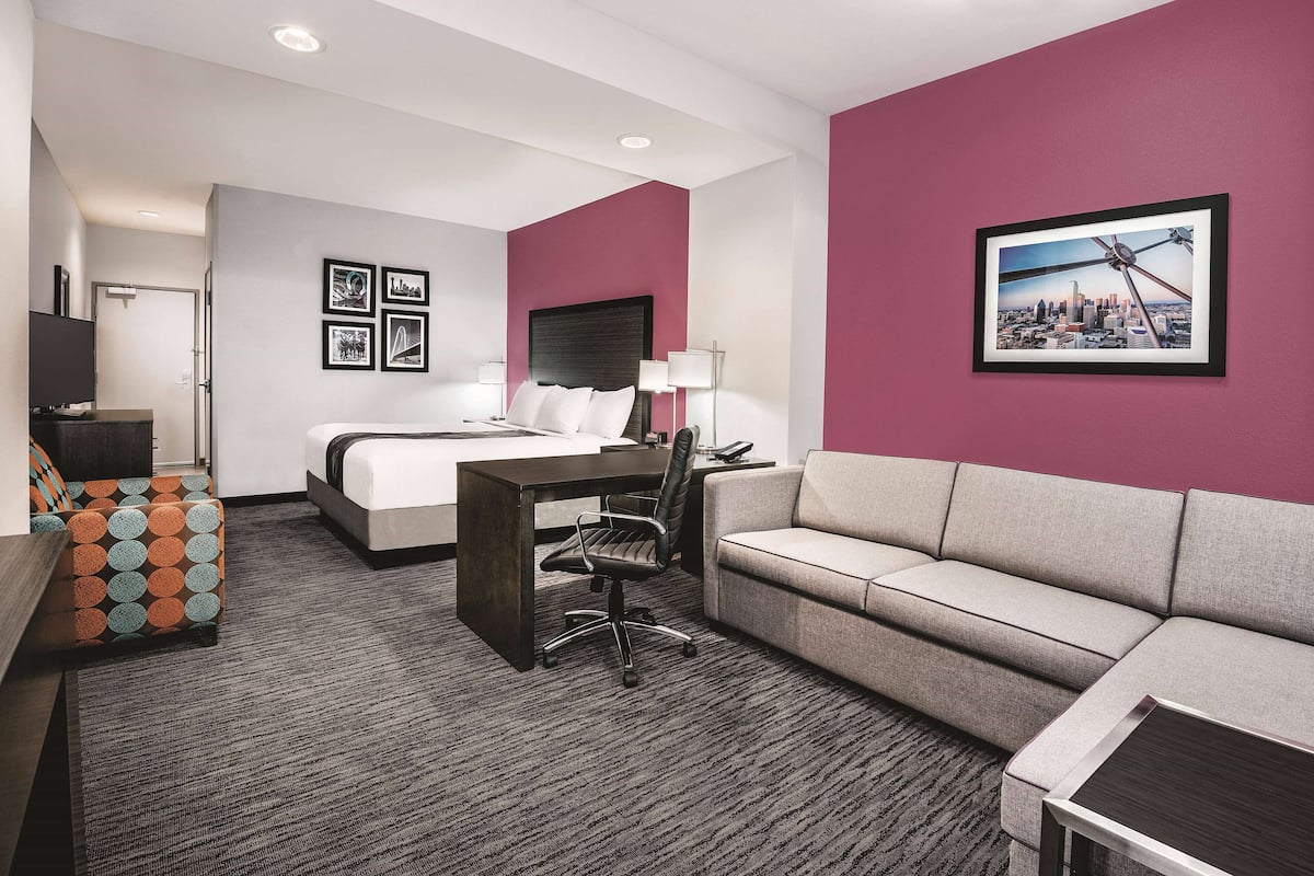 A hotel room with a bed, a desk, a sofa, and a cityscape painting on the wall.