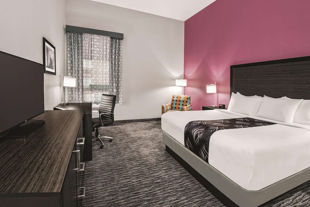 A hotel room with a bed, a desk, a chair, a lamp, and a window with curtains.