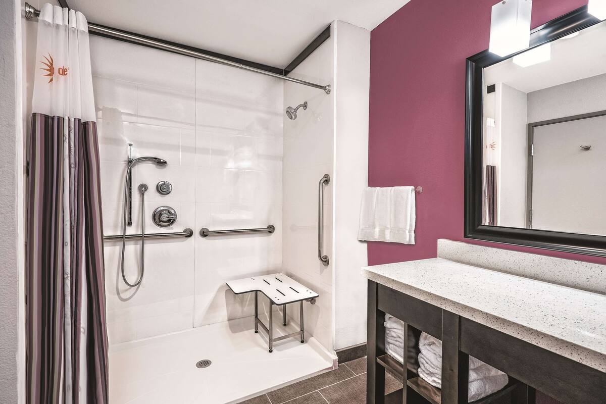 A shower with a grab bar, a small step stool, and a towel rack.