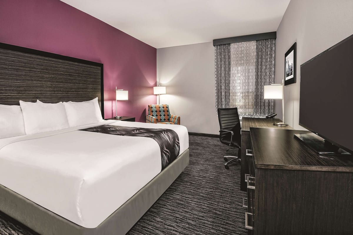 A hotel room with a large bed, a desk, a chair, and a window with patterned curtains.