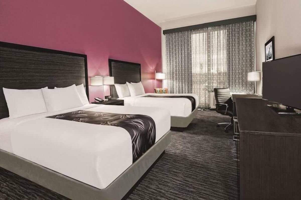 A hotel room with two beds, a desk, a chair, and a TV.