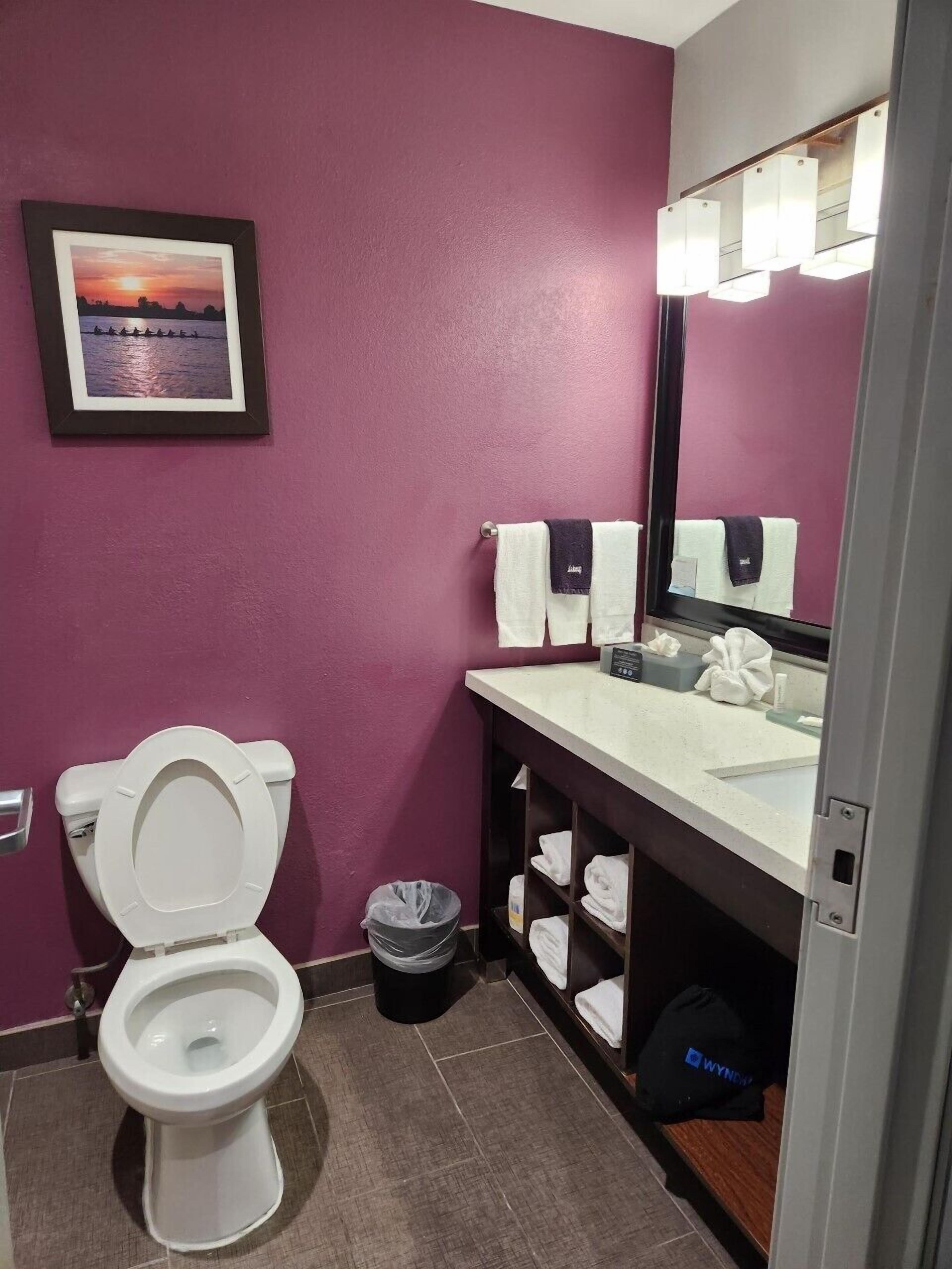 A bathroom with a toilet, a sink with a mirror, and a shelf with towels.