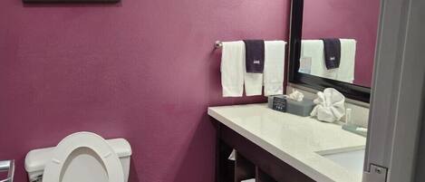 A bathroom with a toilet, a sink with a mirror, and a shelf with towels.