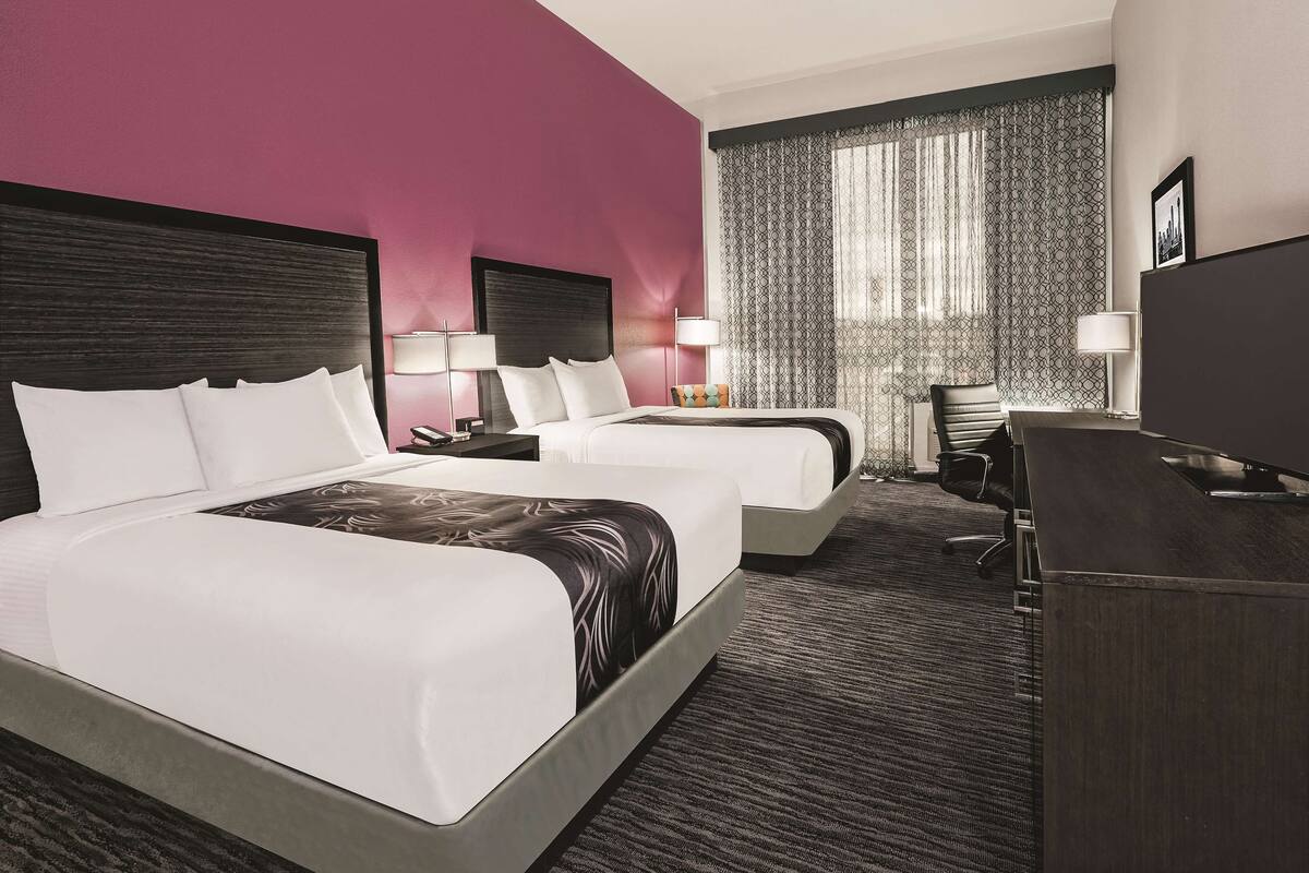 A hotel room with two beds, a desk, and a TV.