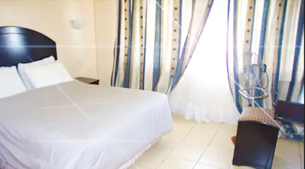 A hotel room with a large bed, a chair, a desk, and curtains.