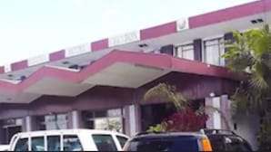 Un edificio con fachada rosa y blanca, múltiples ventanas y un estacionamiento con coches.
