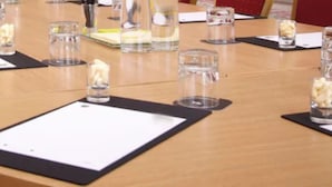 Una mesa de conferencias con cristalería transparente y posavasos negros, preparada para una reunión.
