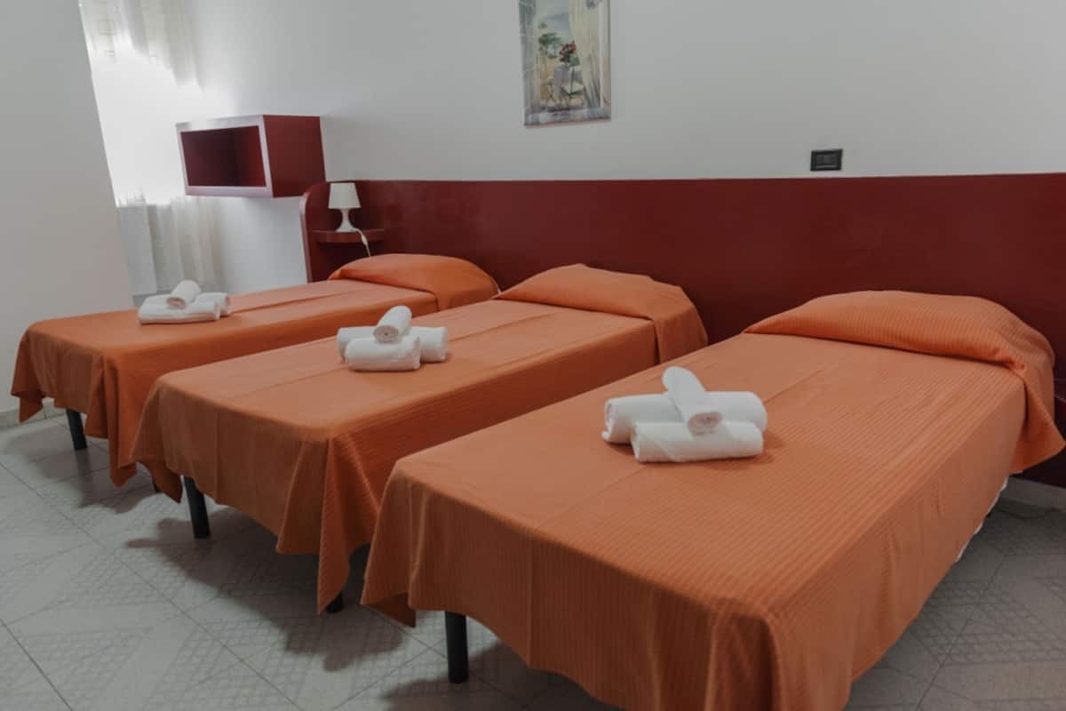 Habitación de hotel con tres camas individuales, cada una con una colcha naranja y una toalla enrollada.